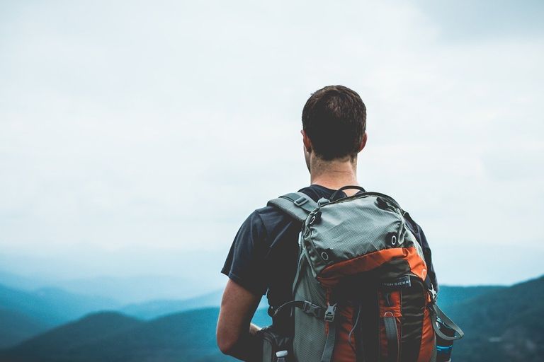 Mann mit Rucksack blickt auf ein weites Bergpanorama