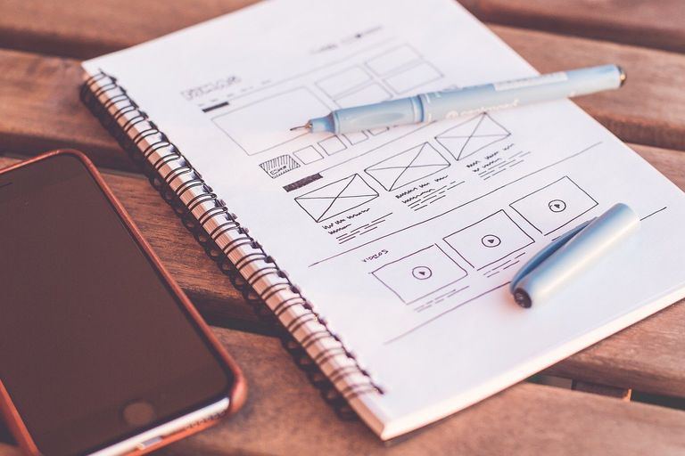Ein Smartphone und daneben ein  Sketchbook mit dem Skribble eines Homepagedesigns