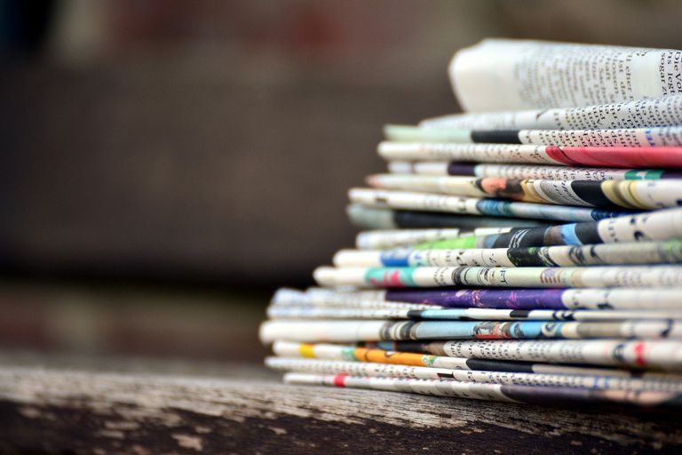 Ein Stapel unterschiedlicher Zeitungen auf einer Holzbank